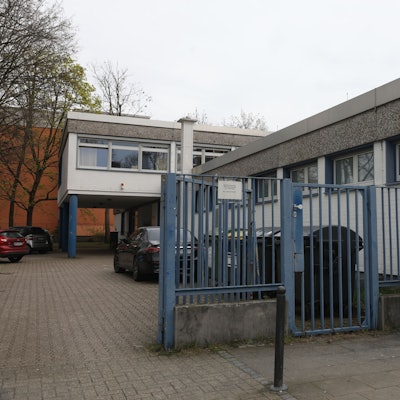 Zu sehen ist eine Kölner Kindertagesstätte von außen mit einem blauen Tor im Vordergrund.