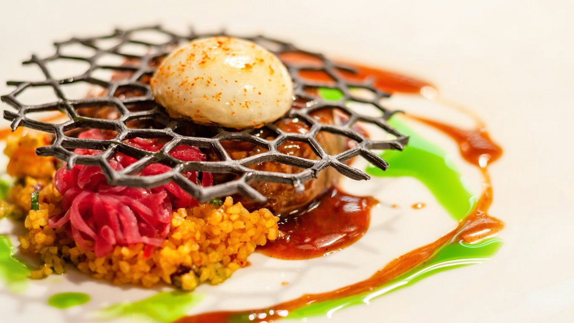 Zu sehen ist eine Hauptspeise aus Lamm und Püree, mit roter und grüne Soße garniert.