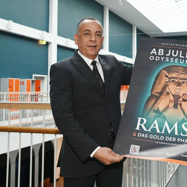 Mostafa Waziri hält in den Gängen des Odysseums Köln ein Plakat der Ausstellung "Ramses & Das Gold der Pharaonen". Die Ausstellung ist ab 13. Juli 2024 zu Gast im Odysseum. Dr. Mostafa Waziri hat sich vor Ort ein Bild gemacht.