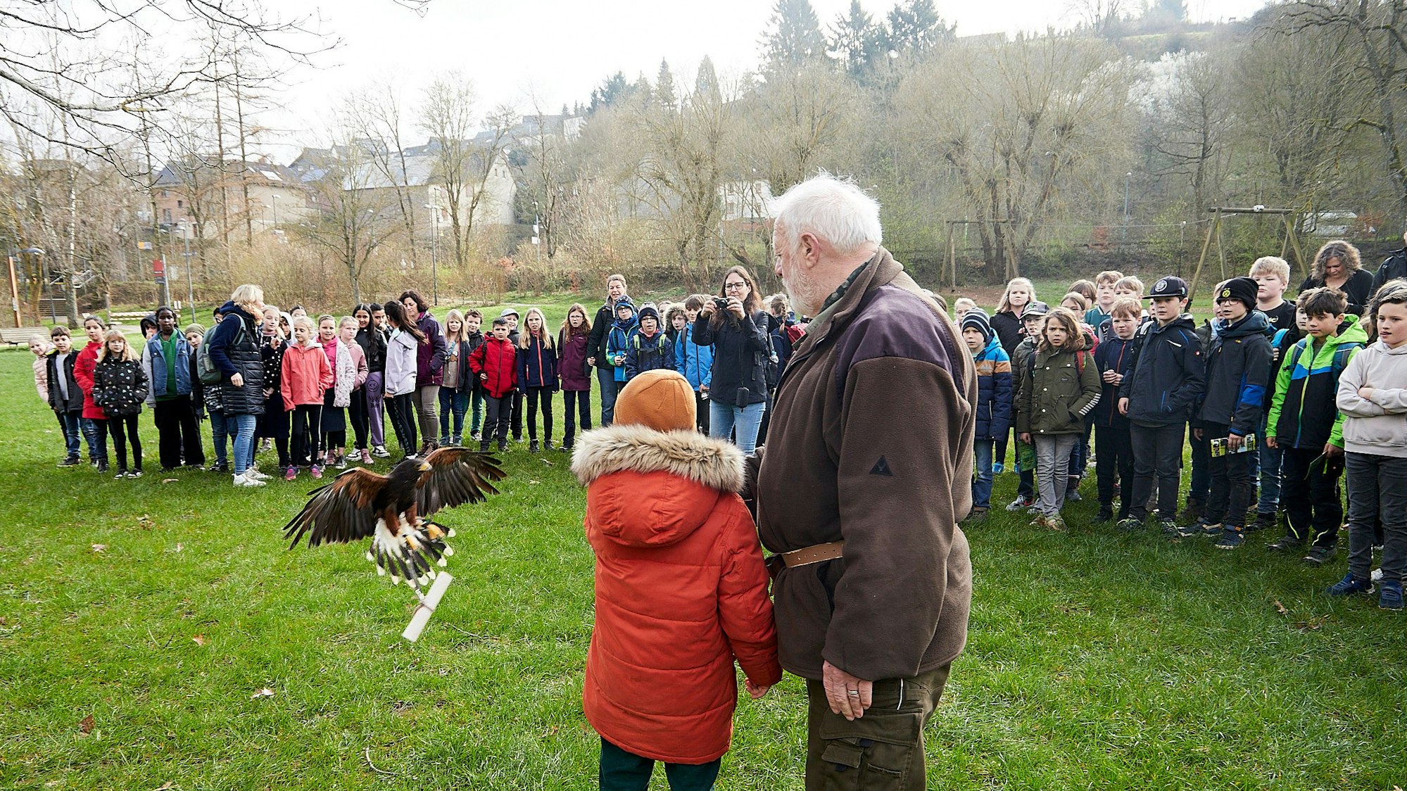Ein Greifvogel fliegt mit einem der Preise in den Klauen auf Karl Fischer vom Wildfreigehege und ein Kind zu. Andere Schülerinnen und Schüler schauen zu.