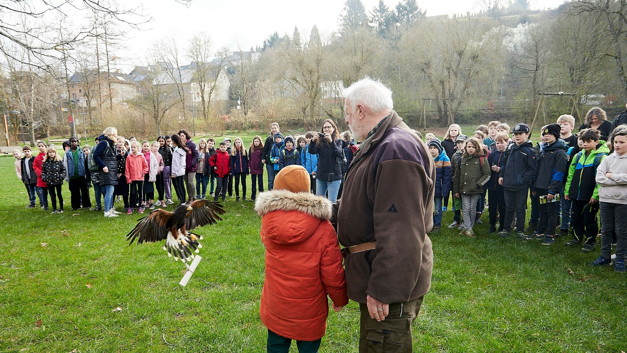 Ein Greifvogel fliegt mit einem der Preise in den Klauen auf Karl Fischer vom Wildfreigehege und ein Kind zu. Andere Schülerinnen und Schüler schauen zu.