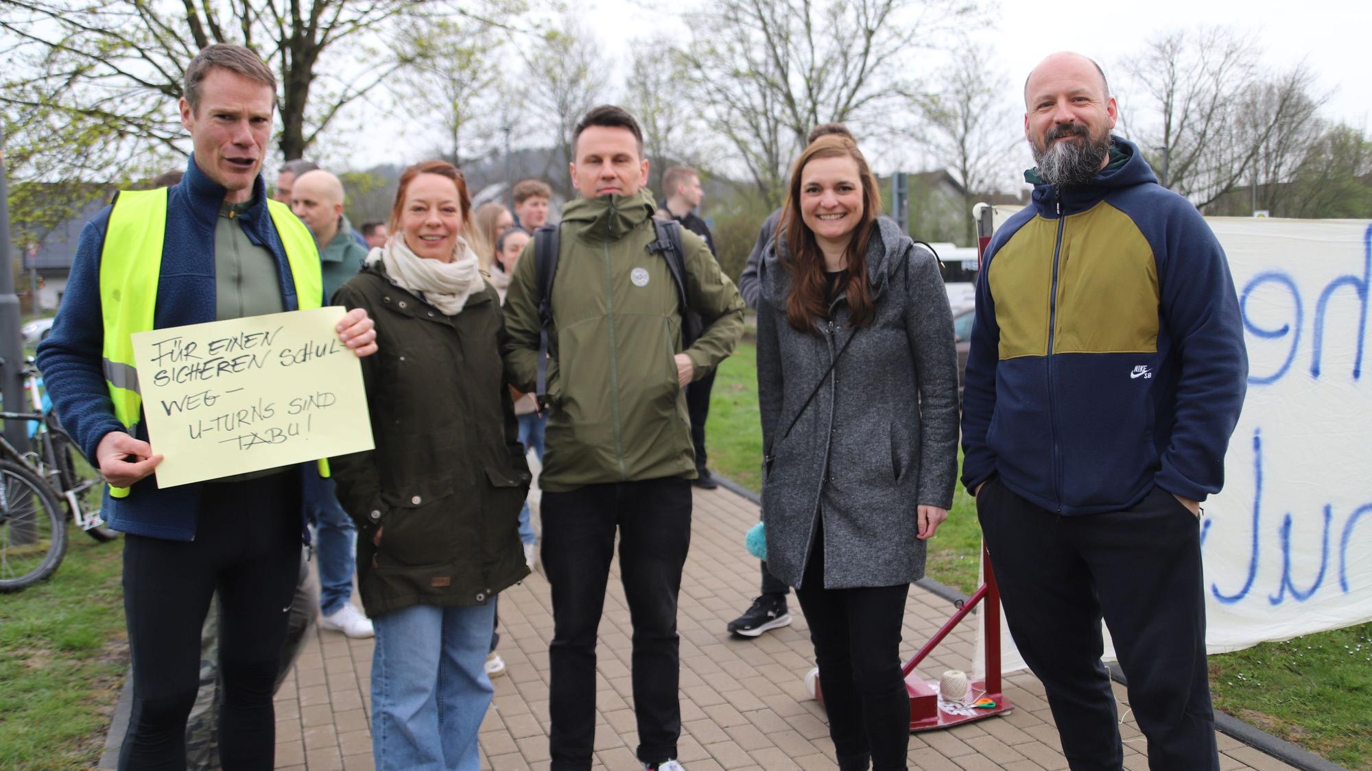 Boris Wolter (l.) hatte aufgerufen. Etliche Mitstreiterinnen und Mitstreiter unterstützen ihn bei seinem Vorhaben. Hier stehen sie auf einem Weg, der zum Gymnasium führt, Wolter hält ein Plakat in den Händen mit der Aufschrift: „Für einen sicheren Schulweg - U-Turns sind tabu!“