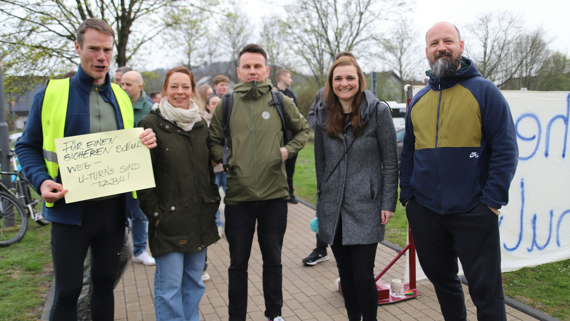 Boris Wolter (l.) hatte aufgerufen. Etliche Mitstreiterinnen und Mitstreiter unterstützen ihn bei seinem Vorhaben. Hier stehen sie auf einem Weg, der zum Gymnasium führt, Wolter hält ein Plakat in den Händen mit der Aufschrift: „Für einen sicheren Schulweg - U-Turns sind tabu!“