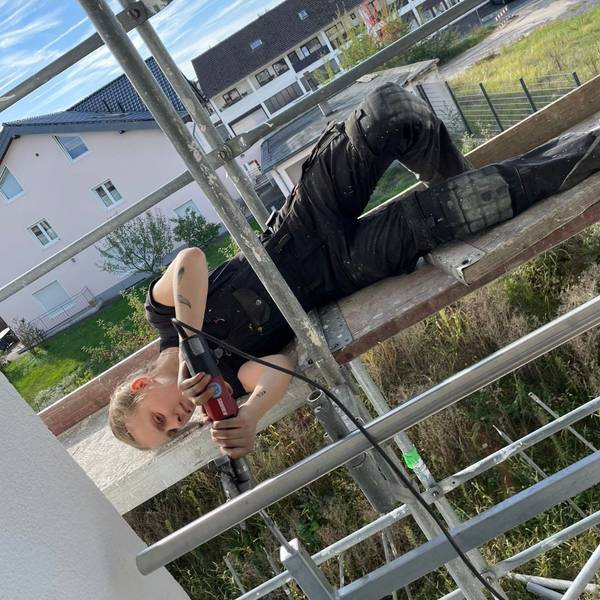Bella Meier liegt auf einem Gerüst und schweißt ein Geländer zusammen.