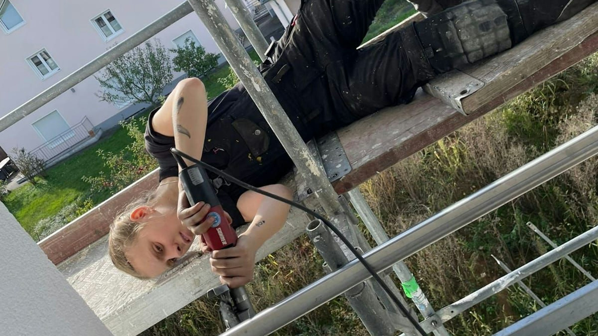 Bella Meier liegt auf einem Gerüst und schweißt ein Geländer zusammen.