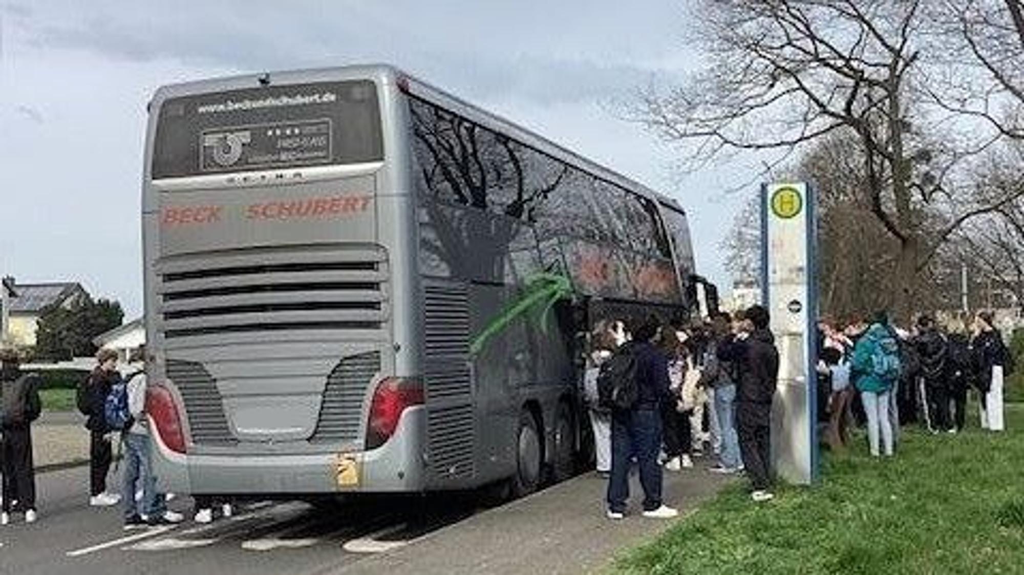 Auf dem Foto sind wartende Schüler vor einem Reisebus zu sehen.
