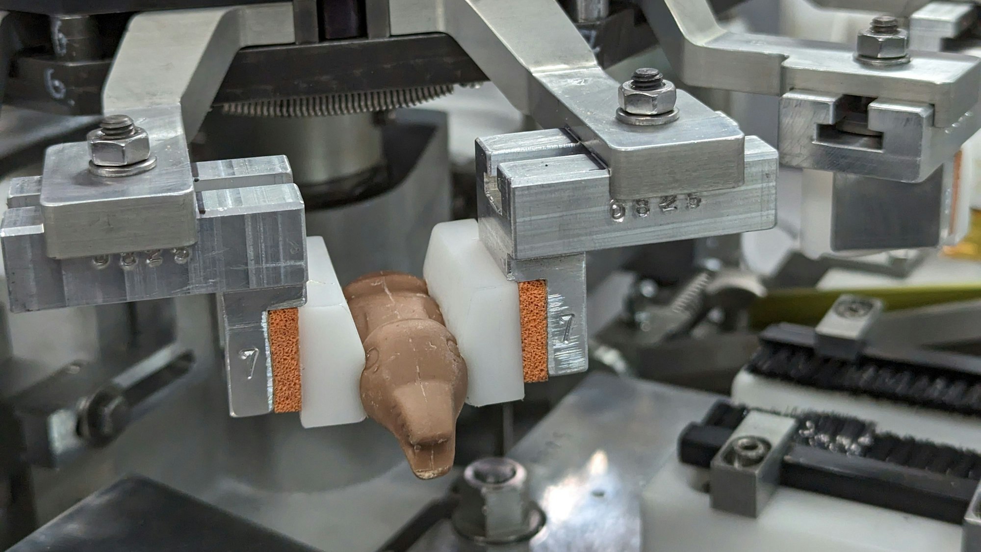 Das Foto zeigt eine Maschine mit vielen beweglichen Metallteilen. Ein kleiner Schokohase ist zwischen zwei Stempeln eingeklemmt.