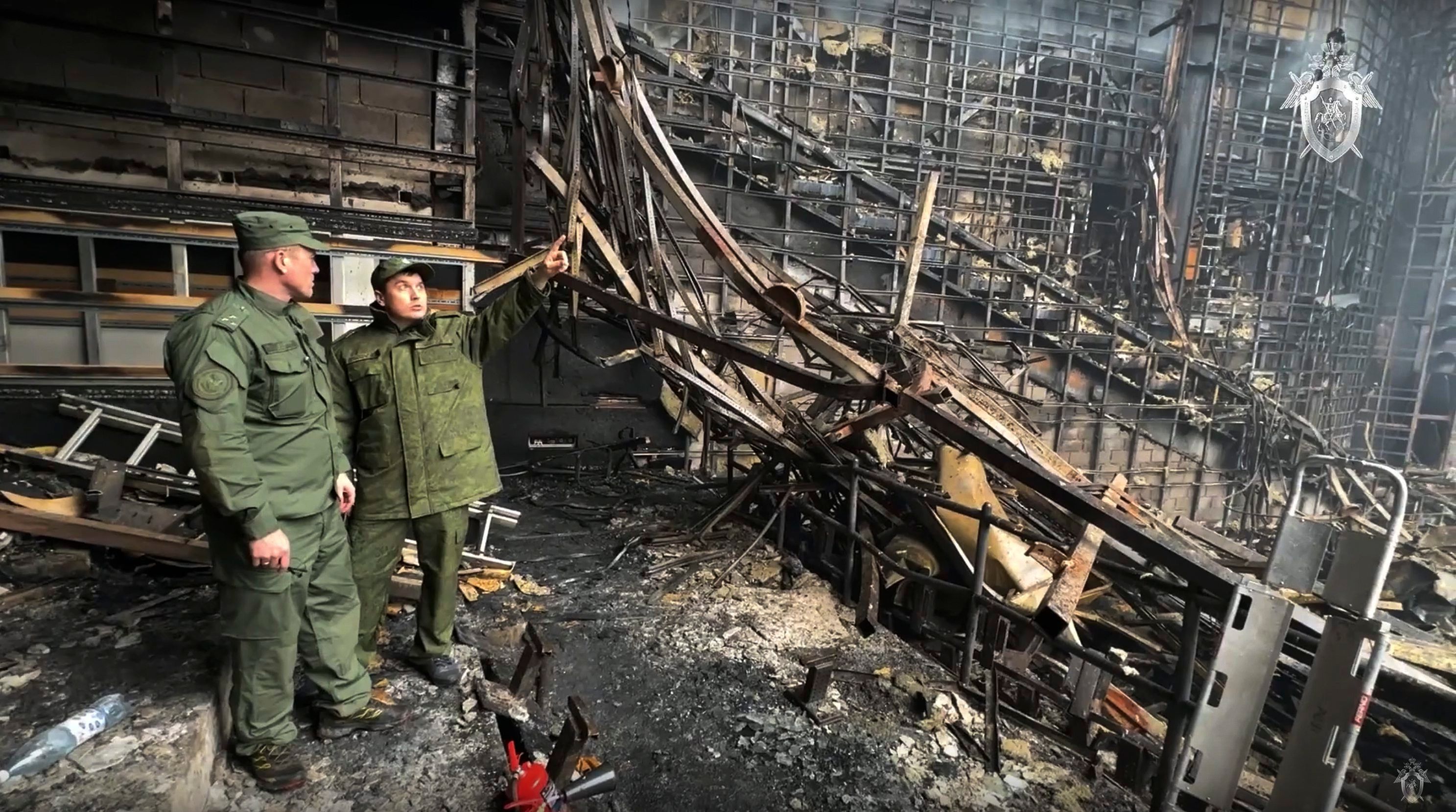 Zwei Männer in russischen Militäruniformen untersuchen das Innere der abgebrannten Veranstaltungshalle Crocus City Hall bei Moskau.