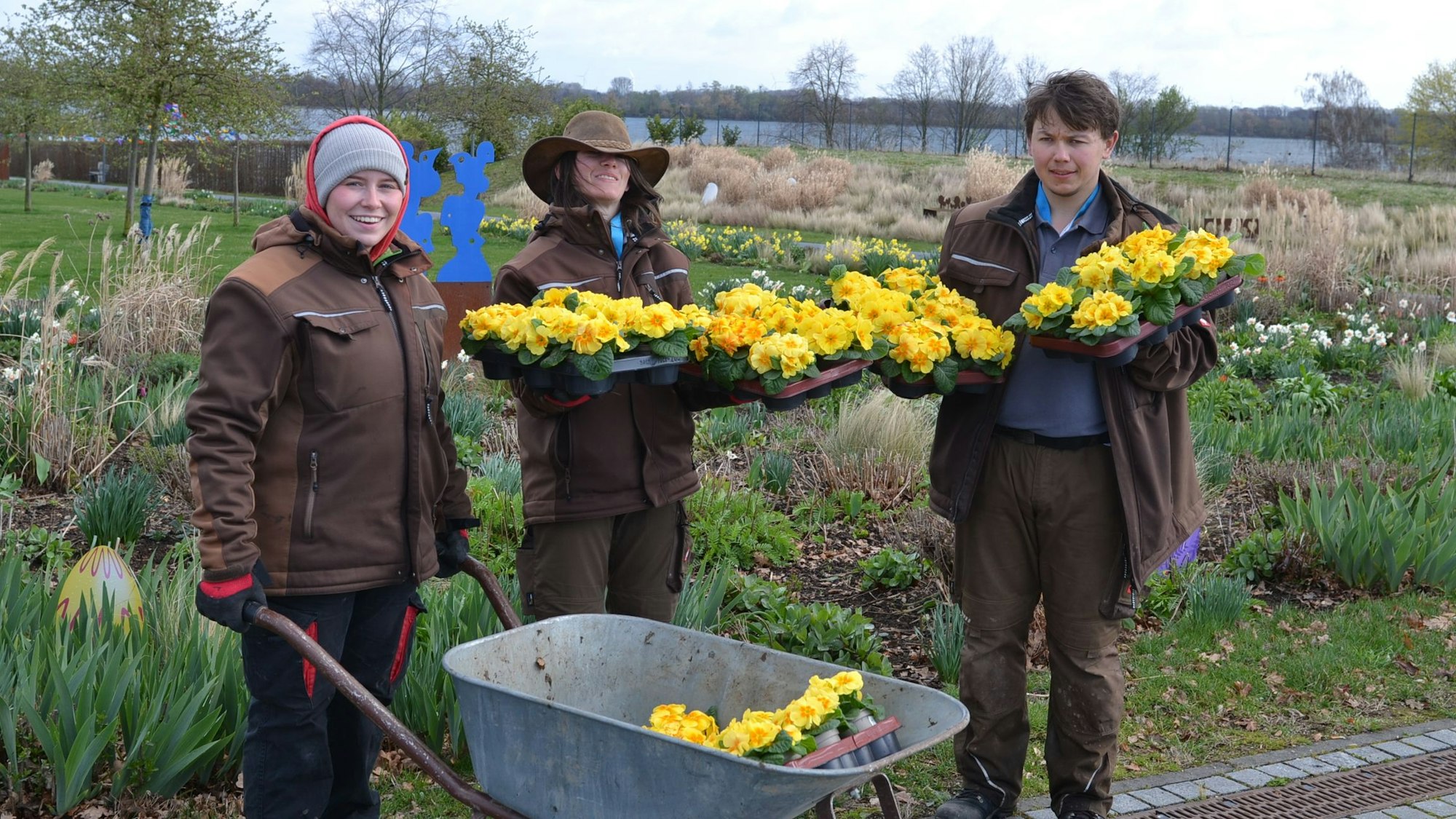 Die drei Helfer sind mit einer Schubkarre voller Stiefmütterchen im Seepark unterwegs.