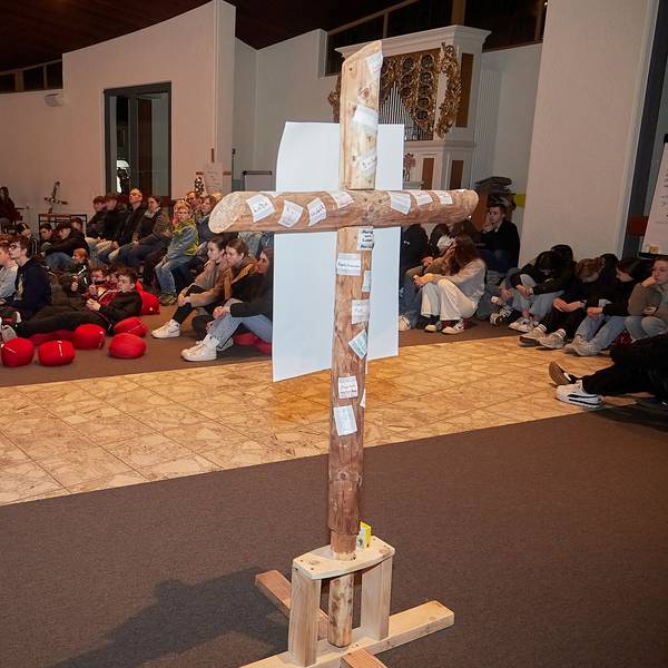 Die Teilnehmer sitzen auf Sitzkissen und auf Stühlen. Im Vordergrund steht ein Kreuz.