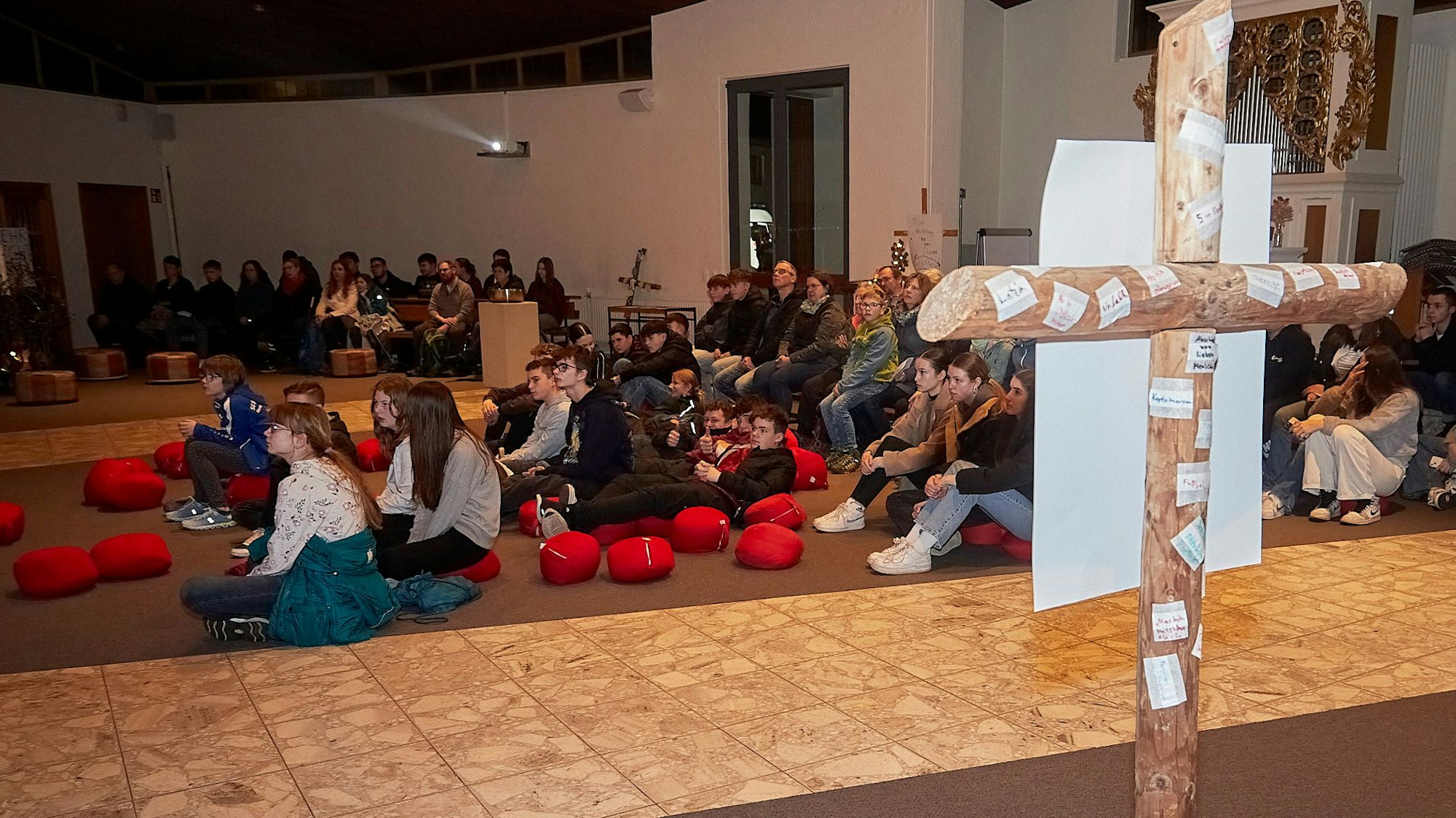 Die Teilnehmer sitzen auf Sitzkissen und auf Stühlen. Im Vordergrund steht ein Kreuz.