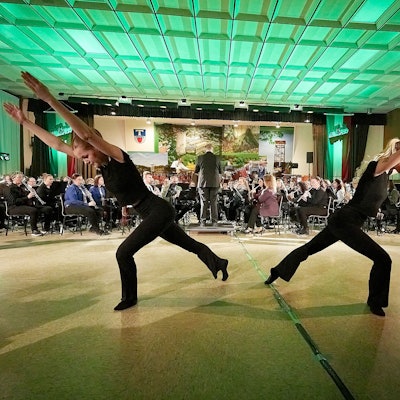 Zwei Tänzerinnen sind im Vordergrund und das Orchester im Hintergrund zu sehen.