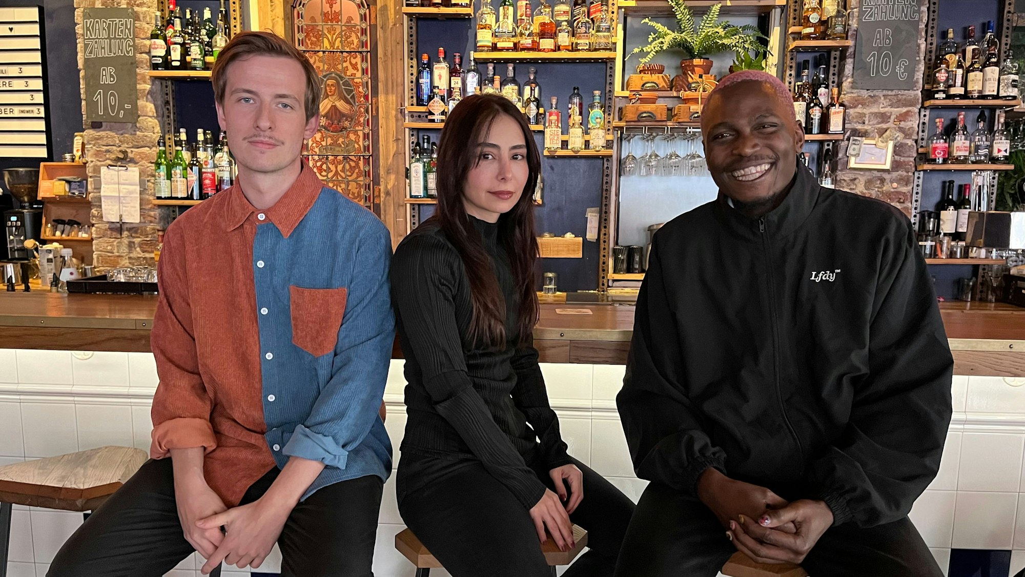 Der Dichter Nico Feiden (l.) sitzt neben Fotografin Zeliha Cambaz (m.) und Veranstalter Davidson Idahosa (r.) an der Bar des Bumann & Sohn.