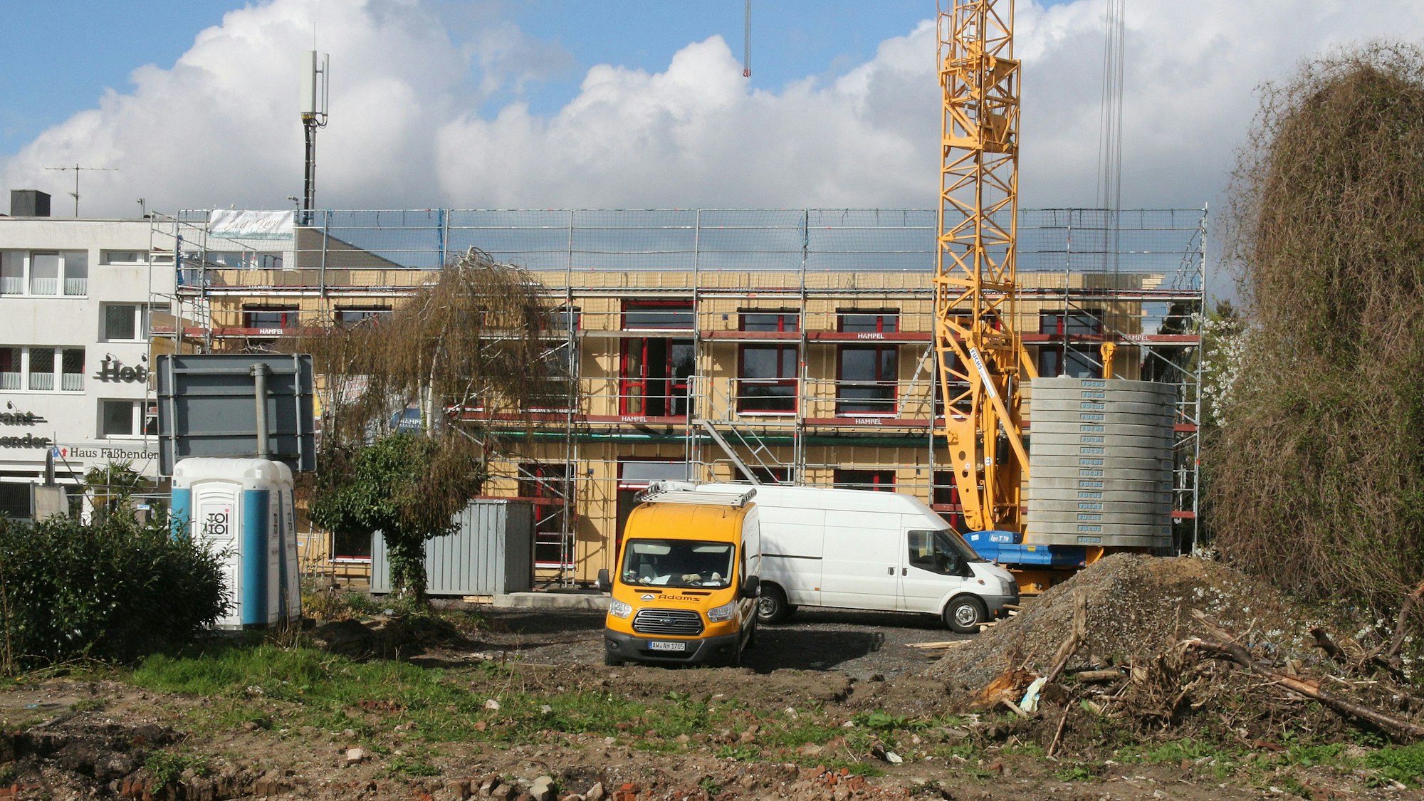 Ein eingerüstetes zweigeschossiges Gebäude, davor stehen zwei Fahrzeuge.