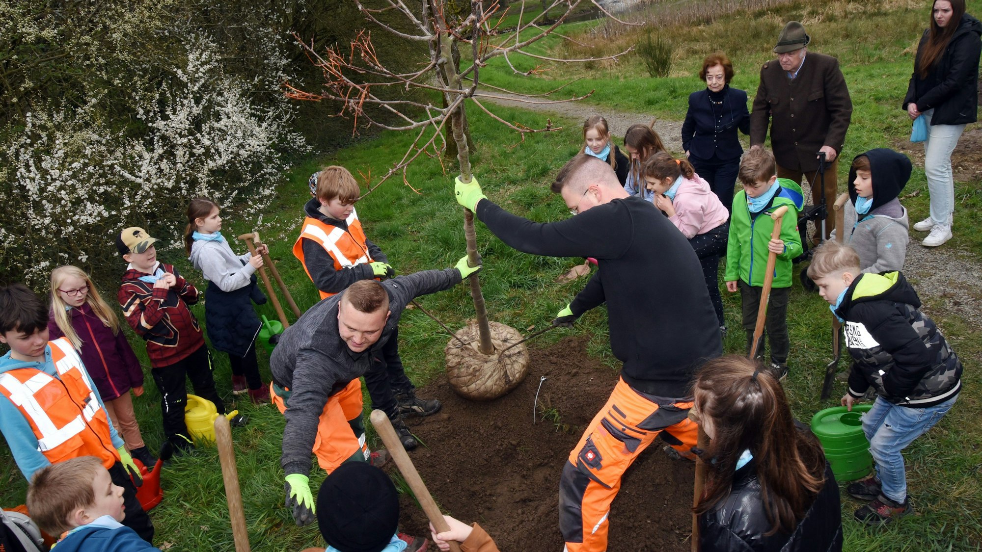 Zwei Männer und viele Kinder pflanzen einen Baum ein.