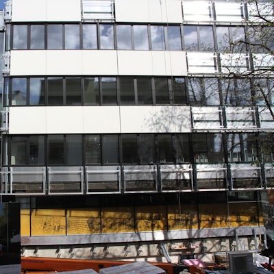 Die Fassade eines Verwaltungsgebäudes, an dem noch einige Fassadenplatten fehlen.