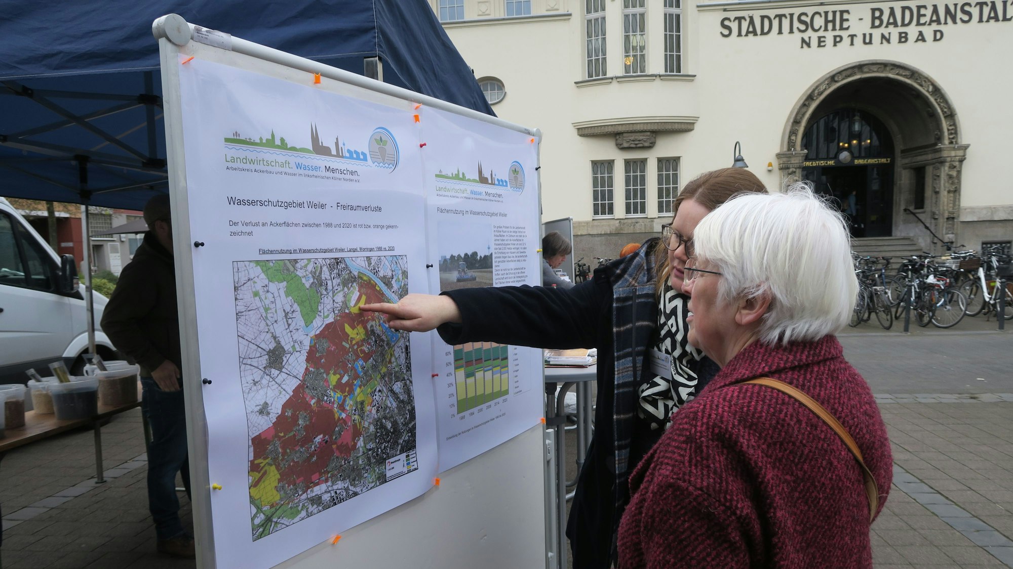 Sarah Thienhaus steht mit einer Passantin auf dem Neptunplatz in Köln-Ehrenfeld. Im Hintergrund ist der Eingang des Neptunbads zu sehen.