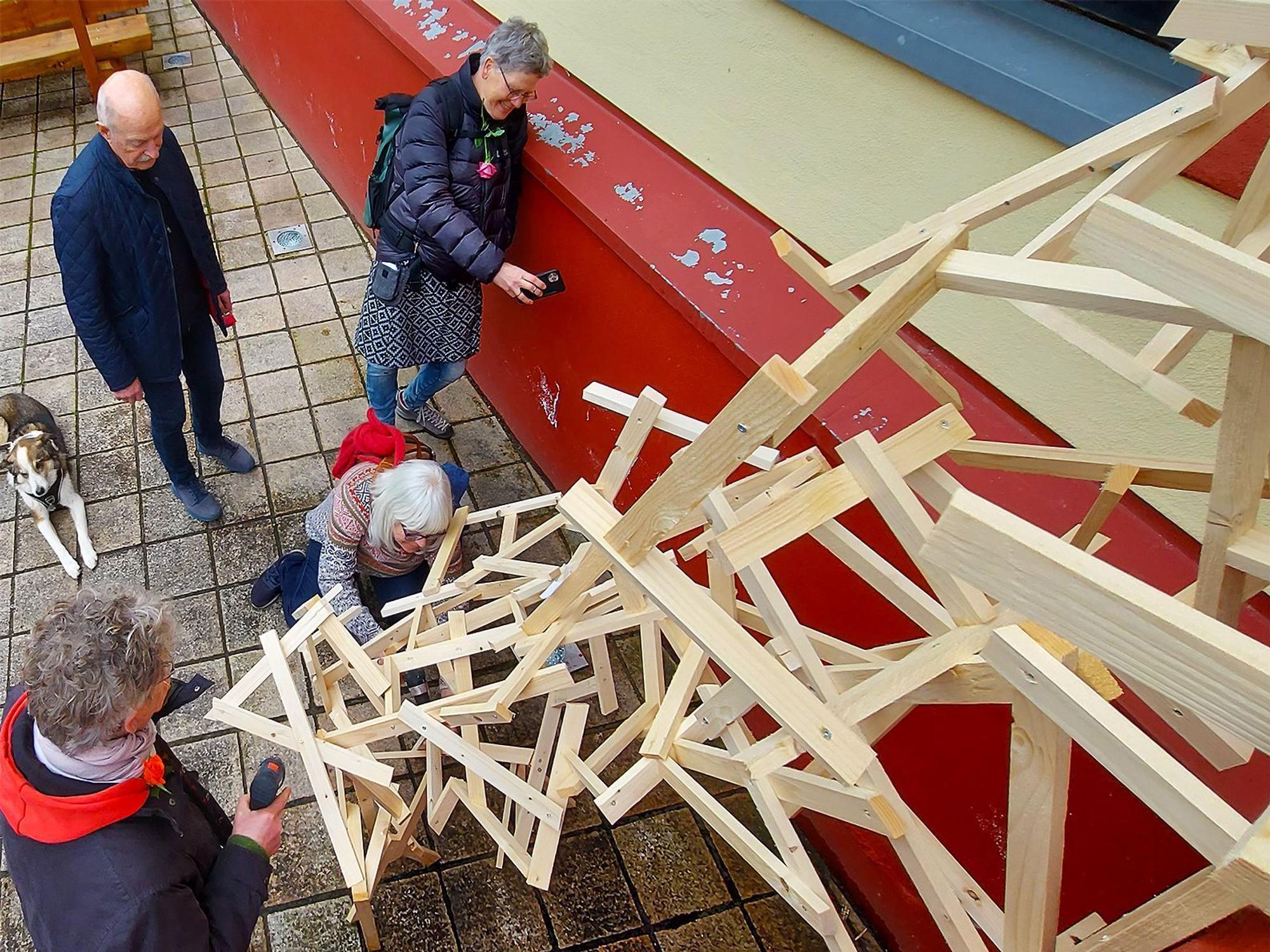 Vier Personen stehen an einer Holzkonstruktion, die die Besucher der aktuellen Ausstellung im Kunstforum in Gemünd gemeinsam gestalteten.