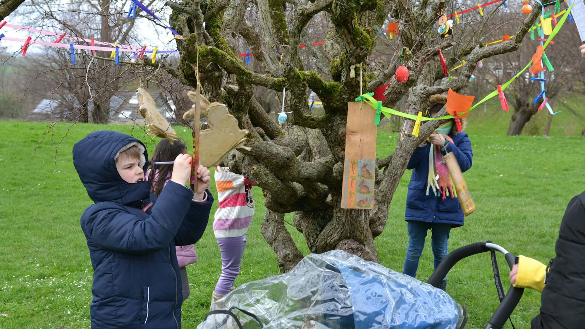 An einem knorrigen Baum hat ein Kind mit einer Wäscheklammer einen Zettel an einer Schnur befestigt. Darauf schreibt es seine Wünsche.