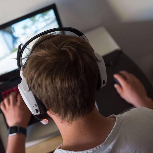 Ein Jugendlicher sitzt mit einem Headset vor einem Laptop und spielt ein Online-Computerspiel.