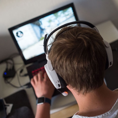 Ein Jugendlicher sitzt mit einem Headset vor einem Laptop und spielt ein Online-Computerspiel.