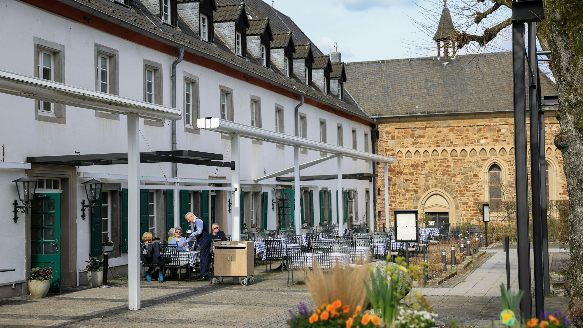 Der Außenbereich des Altenberger-Hofes, es stehen Tische vor einem weißen Haus, im Hintergrund sieht man einen Dom