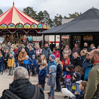 Zwei Artisten auf Stelzen unterhalten beim Jahrmarkt anno dazumal im LVR-Freilichtmuseum Kommern die Besucher. Im Hintergrund sind zwei alte Karussells zu sehen.
