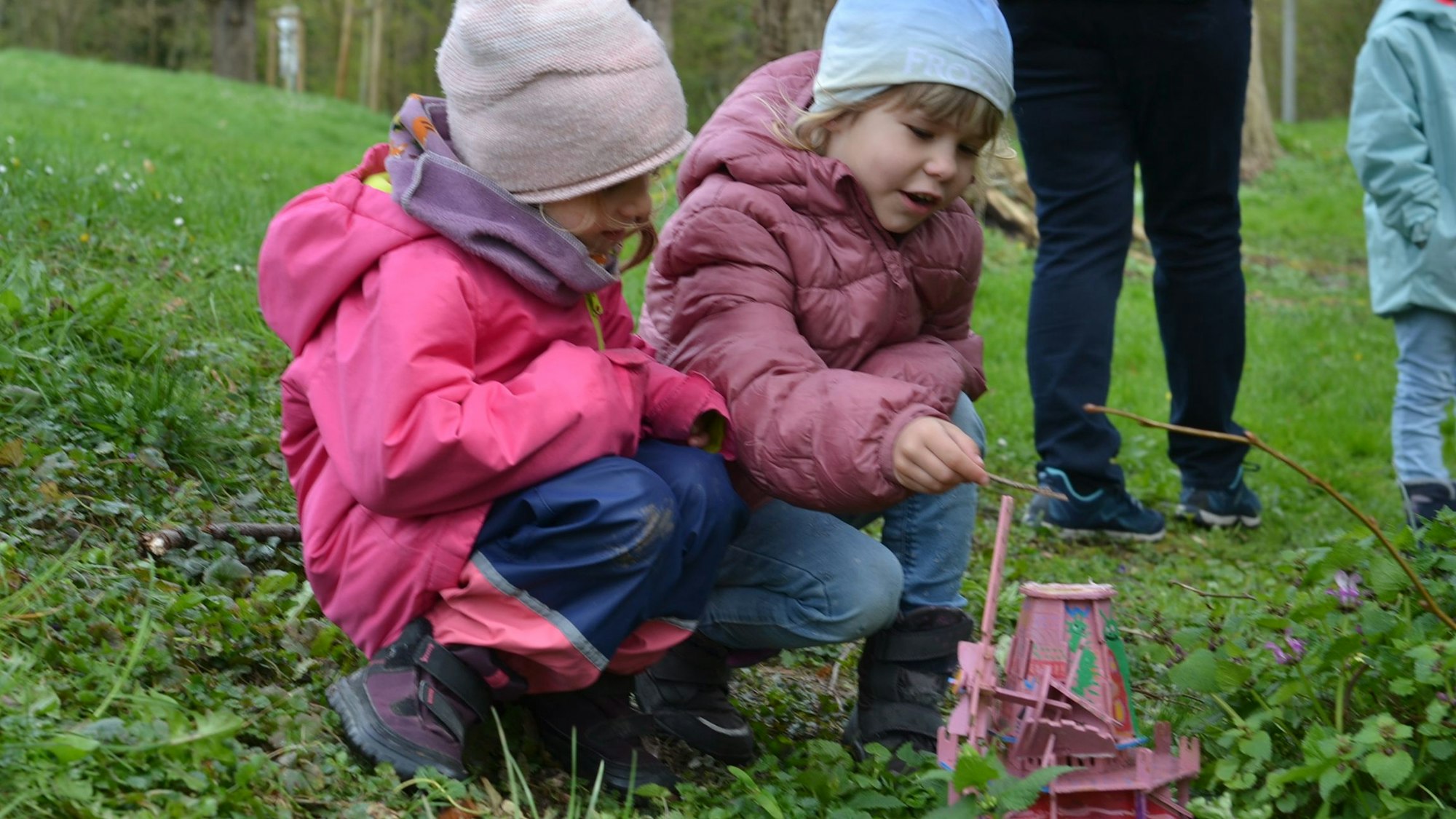 Zwei Mädchen hocken auf einer Wiese und schauen sich eine der Überraschungen auf dem Osterhasenweg an.