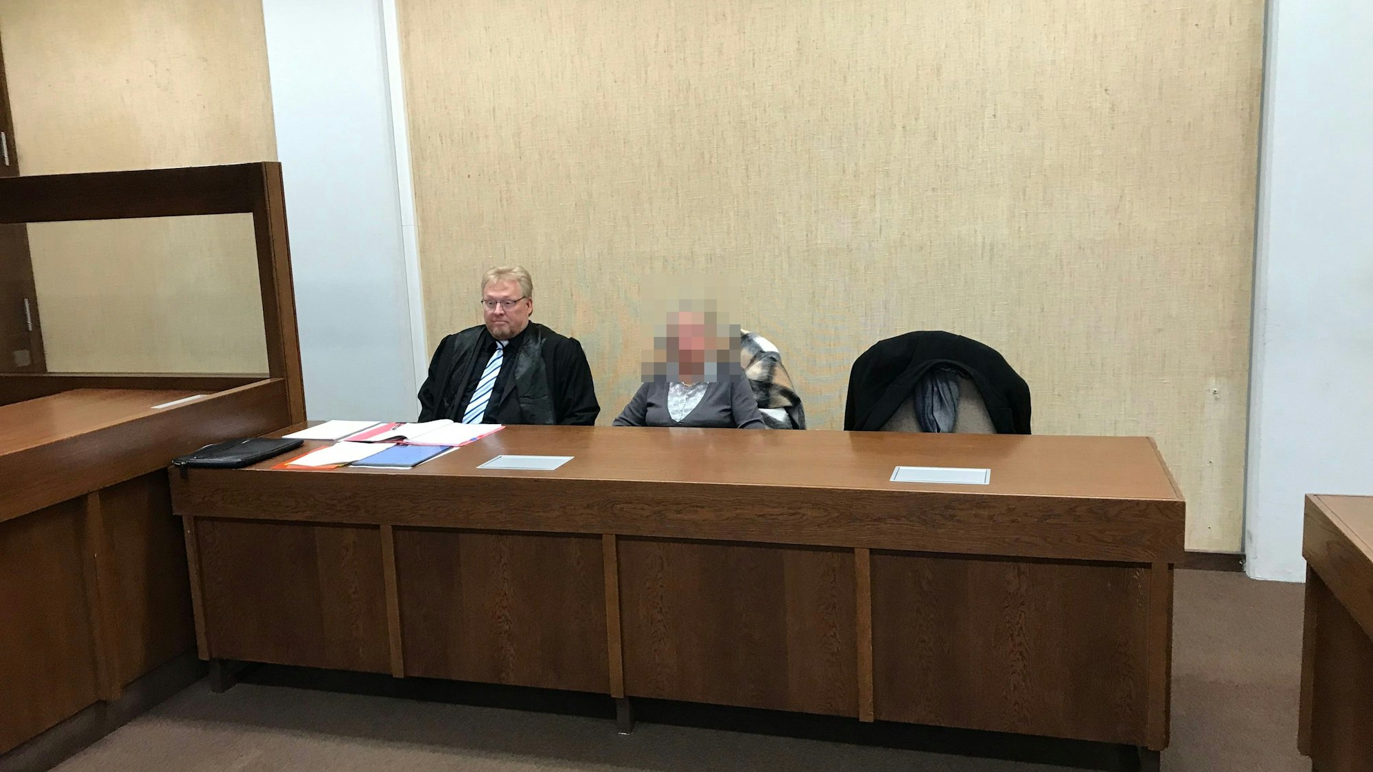 Gepixelte Frau auf einer Anklagebank, links neben ihr sitzt ihr Rechtsanwalt.