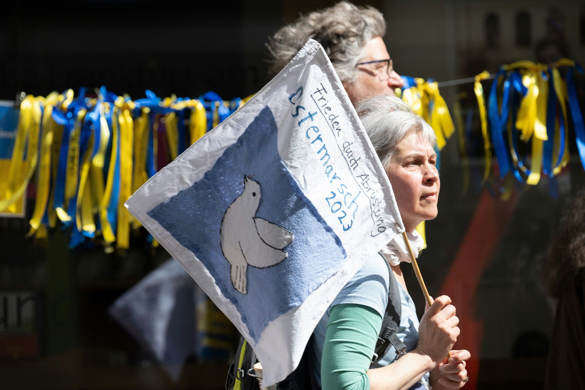ARCHIV - 10.04.2023, Hessen, Frankfurt/Main: Eine Frau mit einer Fahne, auf der «Frieden durch Abrüstung Ostermarsch 2023» steht, geht während eines Ostermarschs an Ukraine-Solidaritätsbändern vorbei. (zu dpa: «Ostermärsche am Wochenende: Linke warnt vor Vereinnahmung durch Rechte») Foto: Sebastian Gollnow/dpa +++ dpa-Bildfunk +++