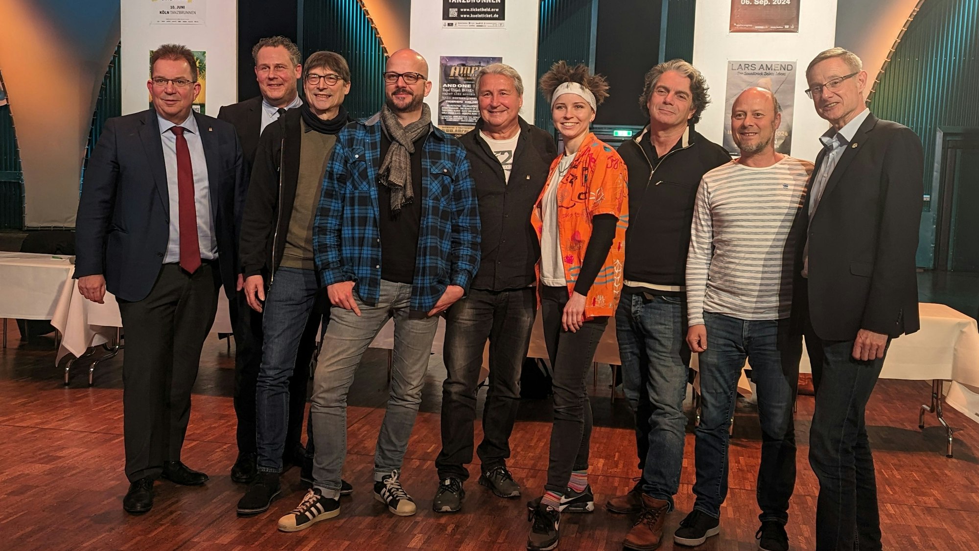 Neun Menschen stehen nebeneinander und schauen in die Kamera.