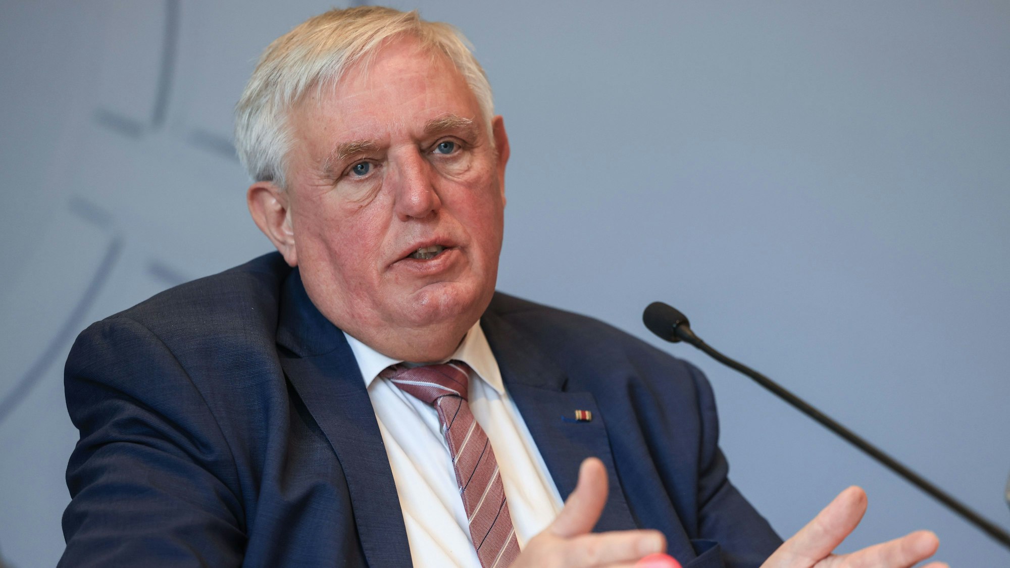 Der NRW-Gesundheitsminister Karl-Josef Laumann (CDU) spricht auf einer Pressekonferenz. Er sitzt im Anzug hinter einem Mikrofon und hat beide Arme gehoben.