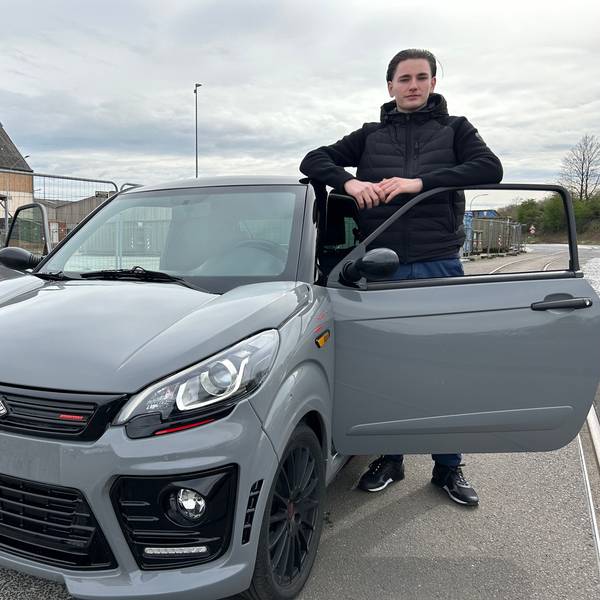Ein Jugendlicher steht angelehnt an die Fahrzeugtür neben seinem Auto.