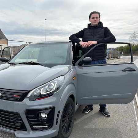 Ein Jugendlicher steht angelehnt an die Fahrzeugtür neben seinem Auto.