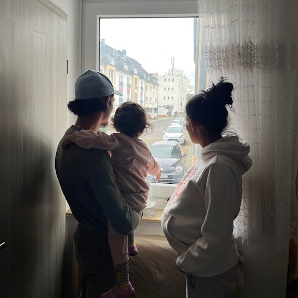 Silhouette einer dreiköpfigen Familie: Vater mit Tochter auf dem Arm, Mutter rechts, gucken aus dem Fenster