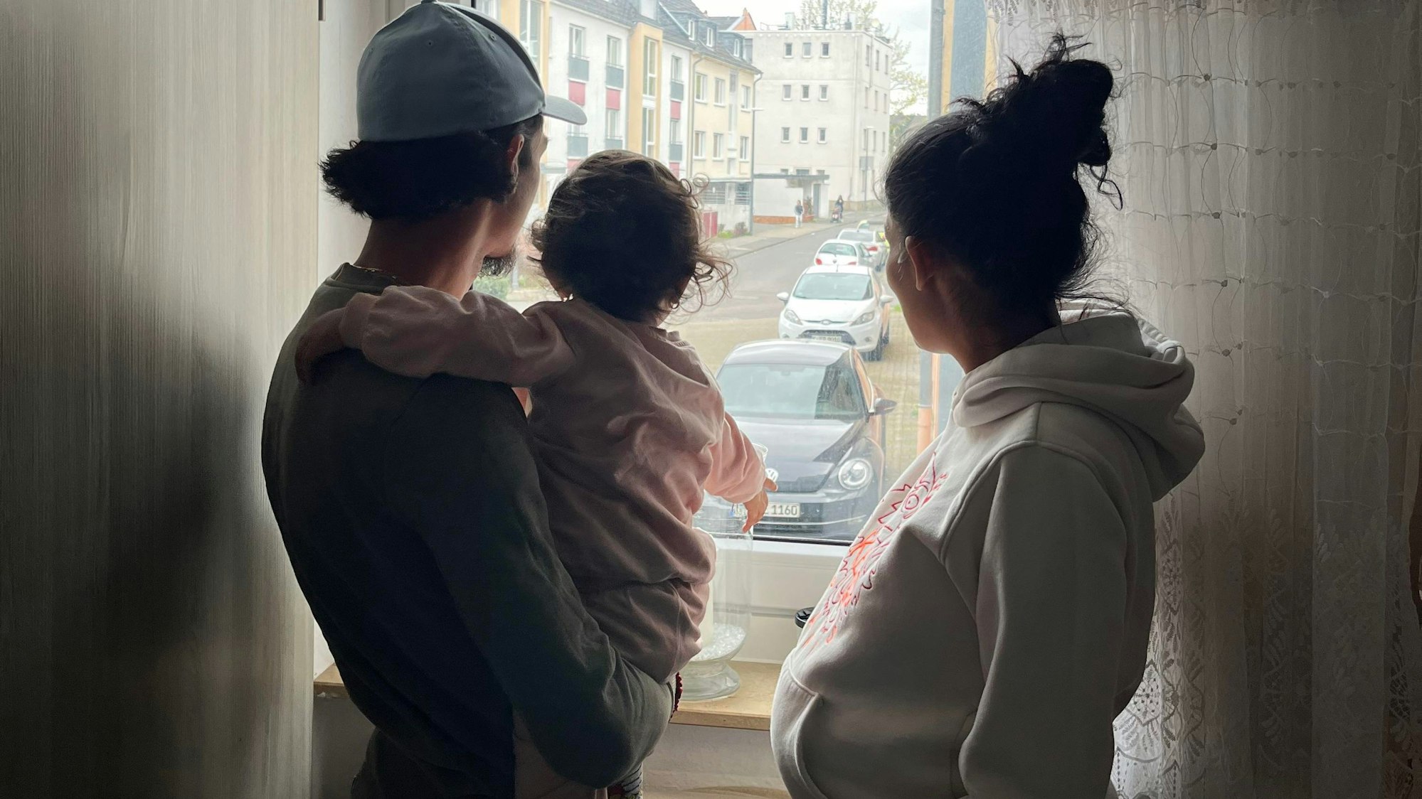 Silhouette einer dreiköpfigen Familie: Vater mit Tochter auf dem Arm, Mutter rechts, gucken aus dem Fenster