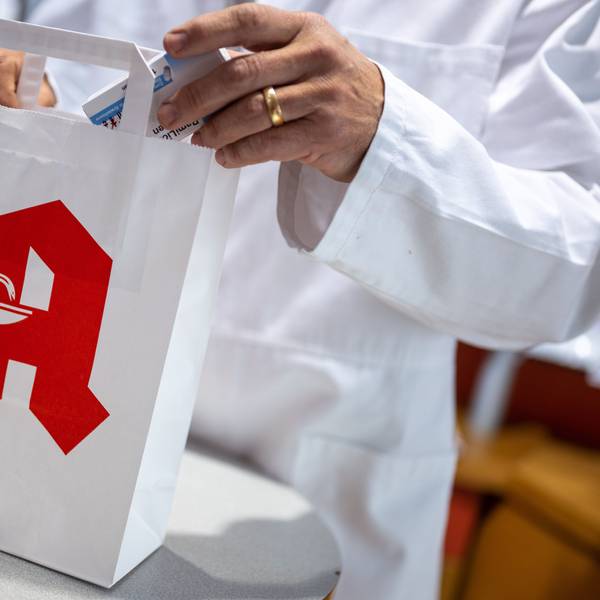Ein Apotheker legt in einer Apotheke eine Packung mit Tabletten in eine Papiertasche mit Apotheken-Logo.