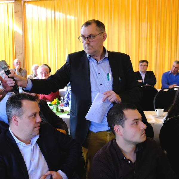 Ein Besucher einer Diskussionsveranstaltung gestikuliert, während ihm der Moderator ein Mikrofon entgegenstreckt.