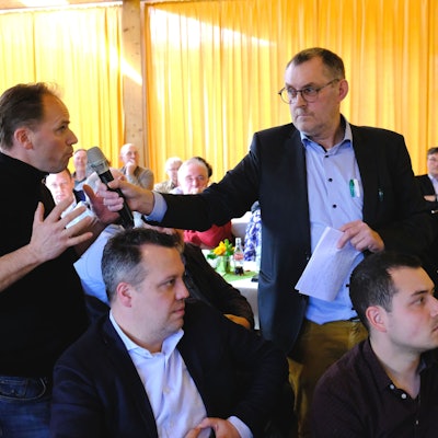 Ein Besucher einer Diskussionsveranstaltung gestikuliert, während ihm der Moderator ein Mikrofon entgegenstreckt.