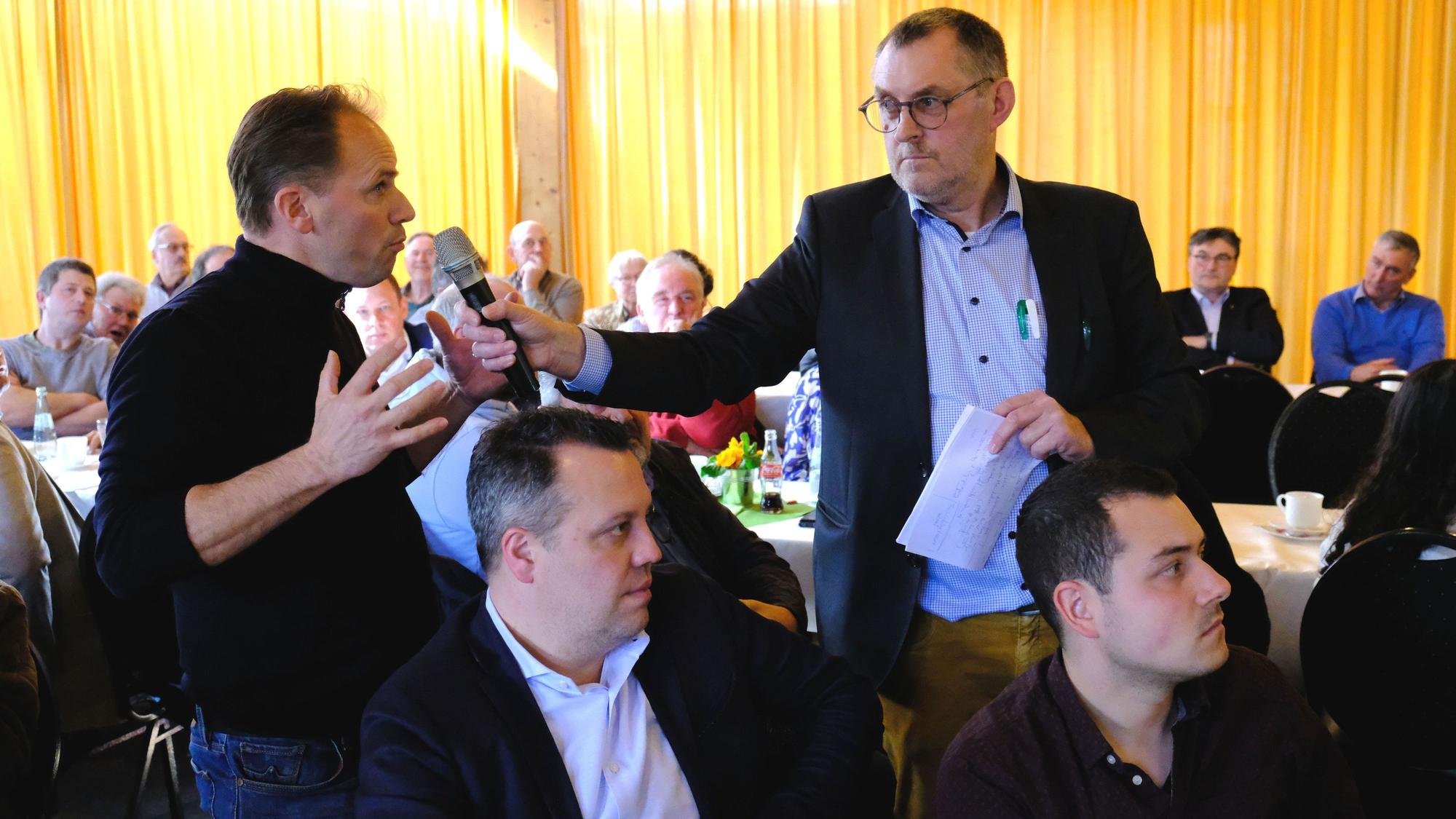 Ein Besucher einer Diskussionsveranstaltung gestikuliert, während ihm der Moderator ein Mikrofon entgegenstreckt.