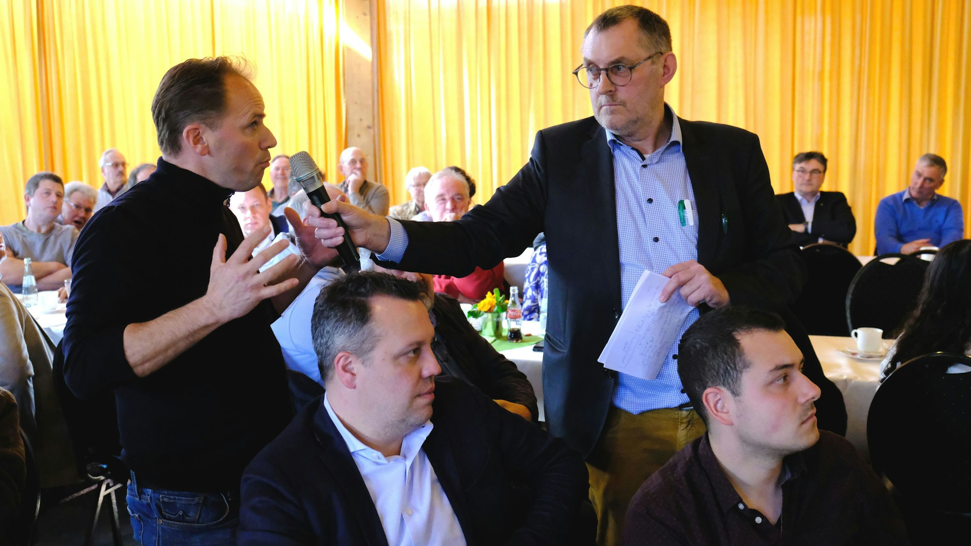 Ein Besucher einer Diskussionsveranstaltung gestikuliert, während ihm der Moderator ein Mikrofon entgegenstreckt.