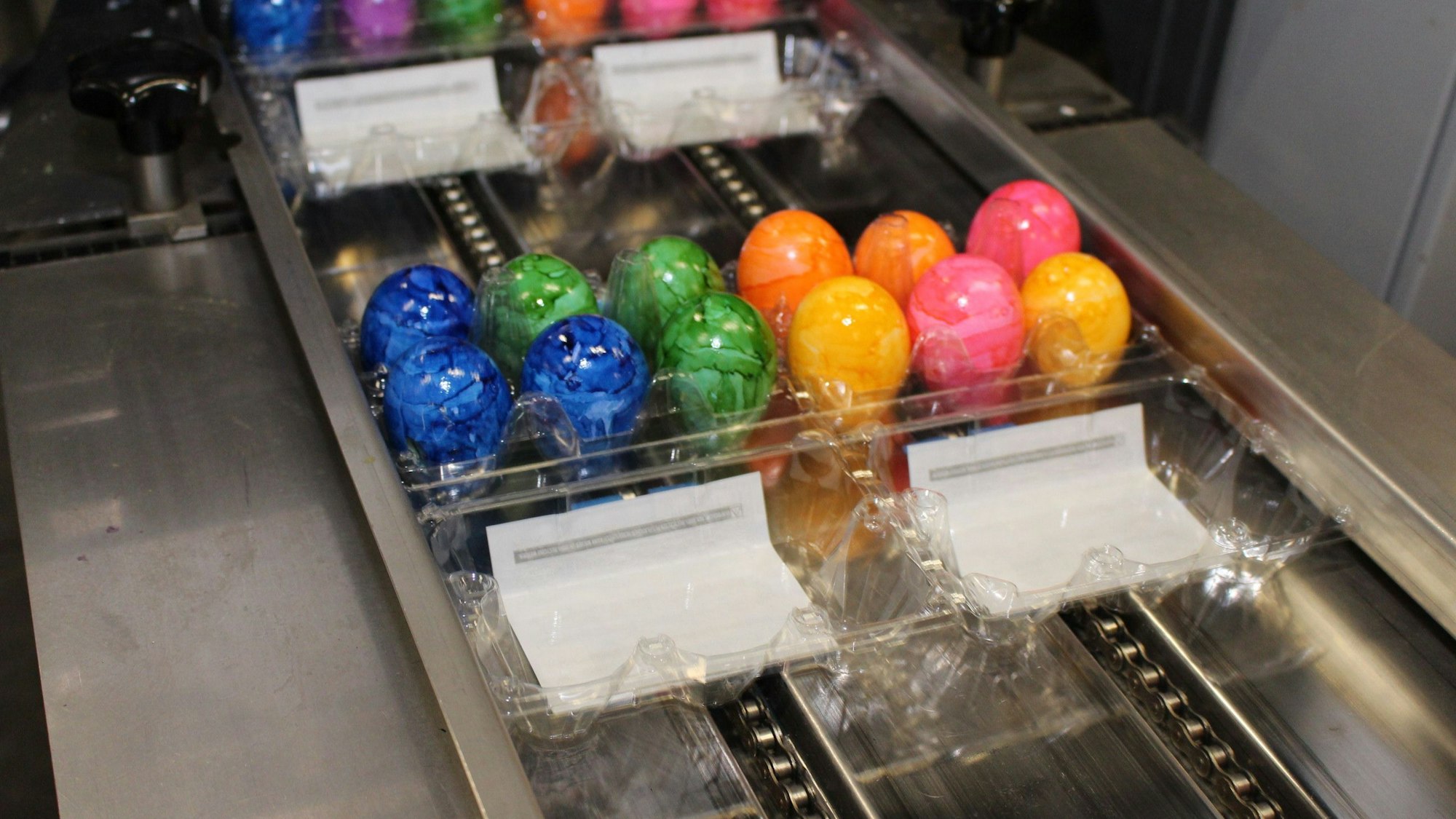 Eine Packung mit bunten Eiern auf einem Förderband.