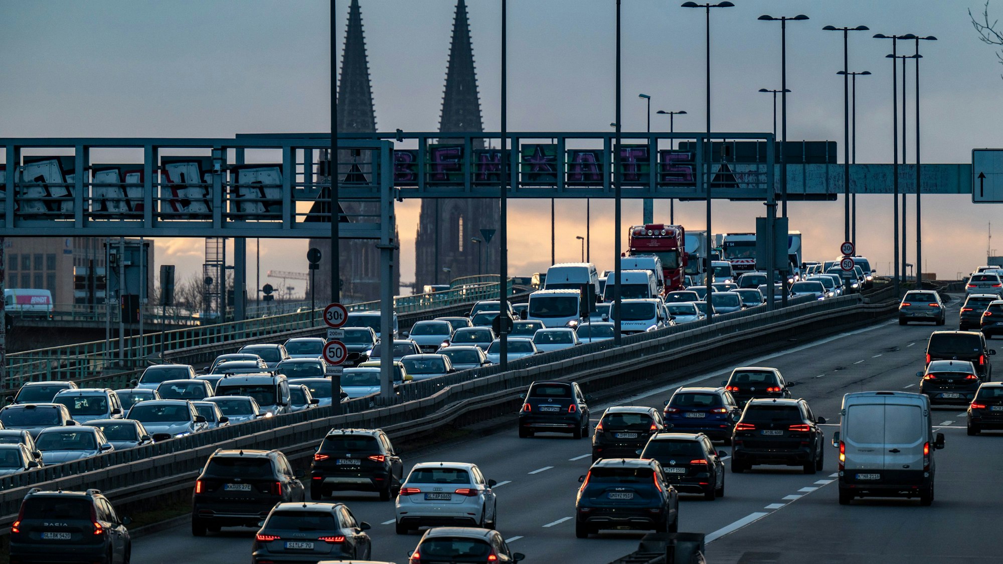 Autos stehen auf einer Brücke im Stau, im Hintergrund ist der Kölner Dom zu sehen.