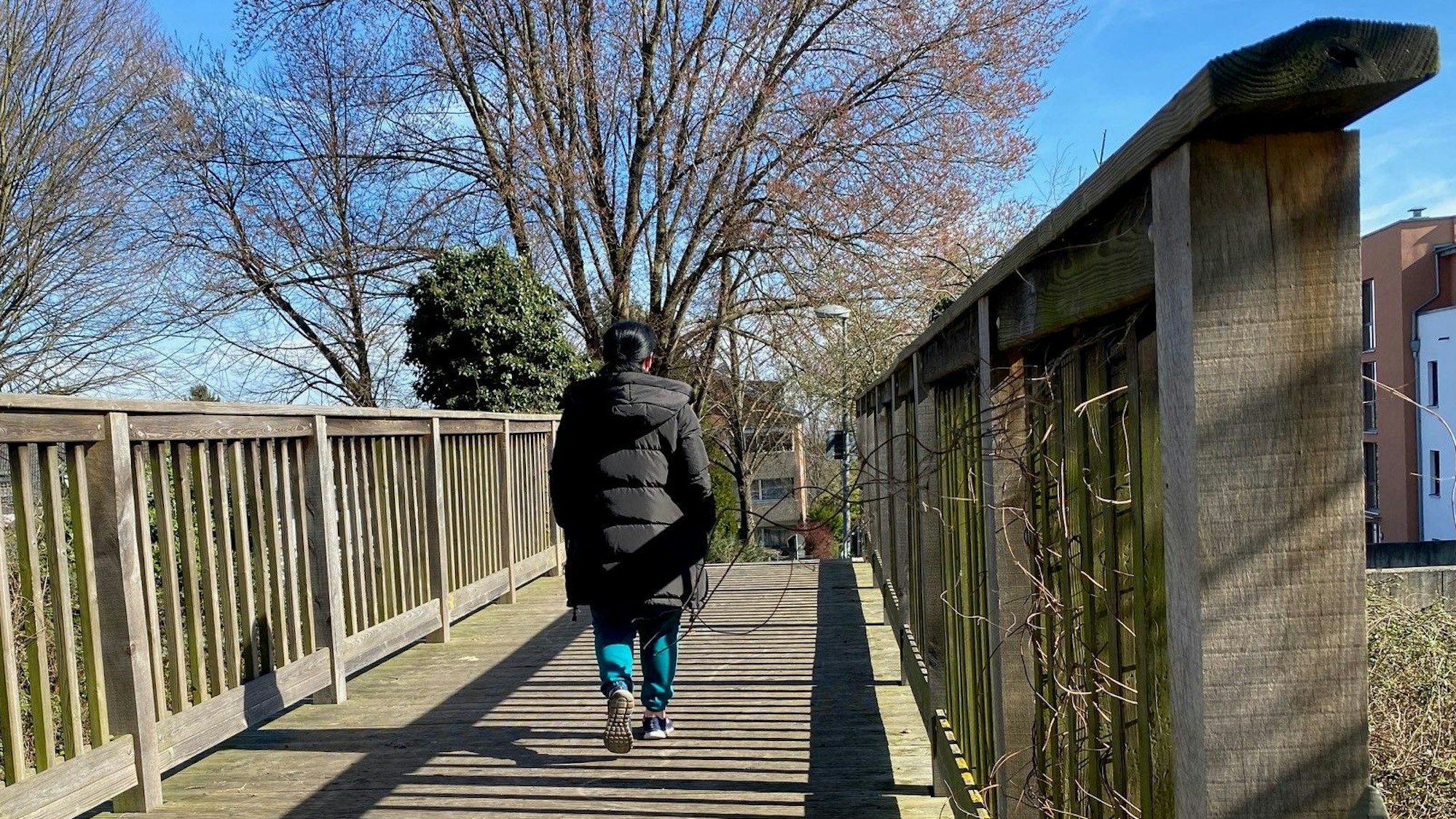 Das Bild zeigt eine Holzbrücke, über die eine Person spaziert.