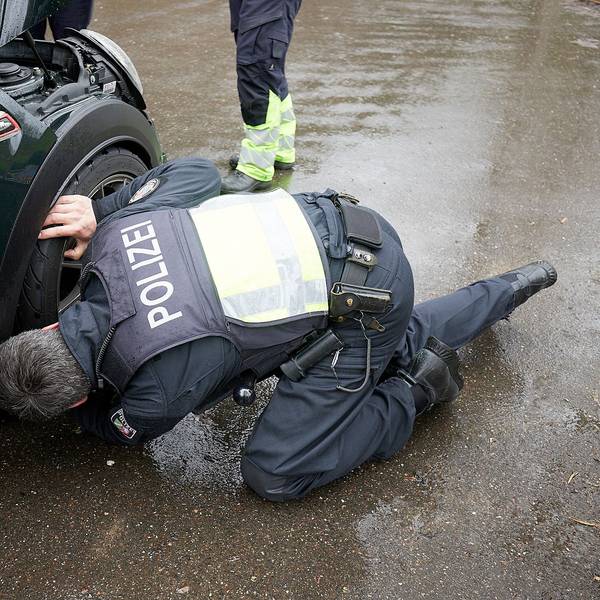 Ein Polizist kniet an einem Sportwagen und kontrolliert die Reifen.