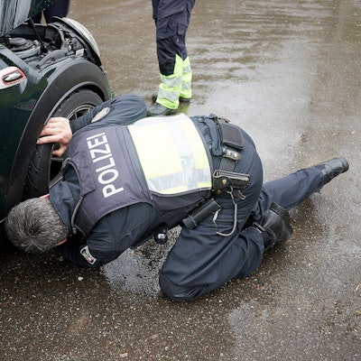 Ein Polizist kniet an einem Sportwagen und kontrolliert die Reifen.