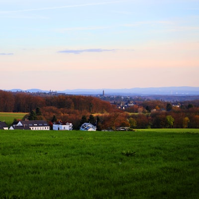 Am Horizont eines Landschaftsbildes sind Schlosstürme und eine Kirche sowie Berge in der Ferne zu sehen.