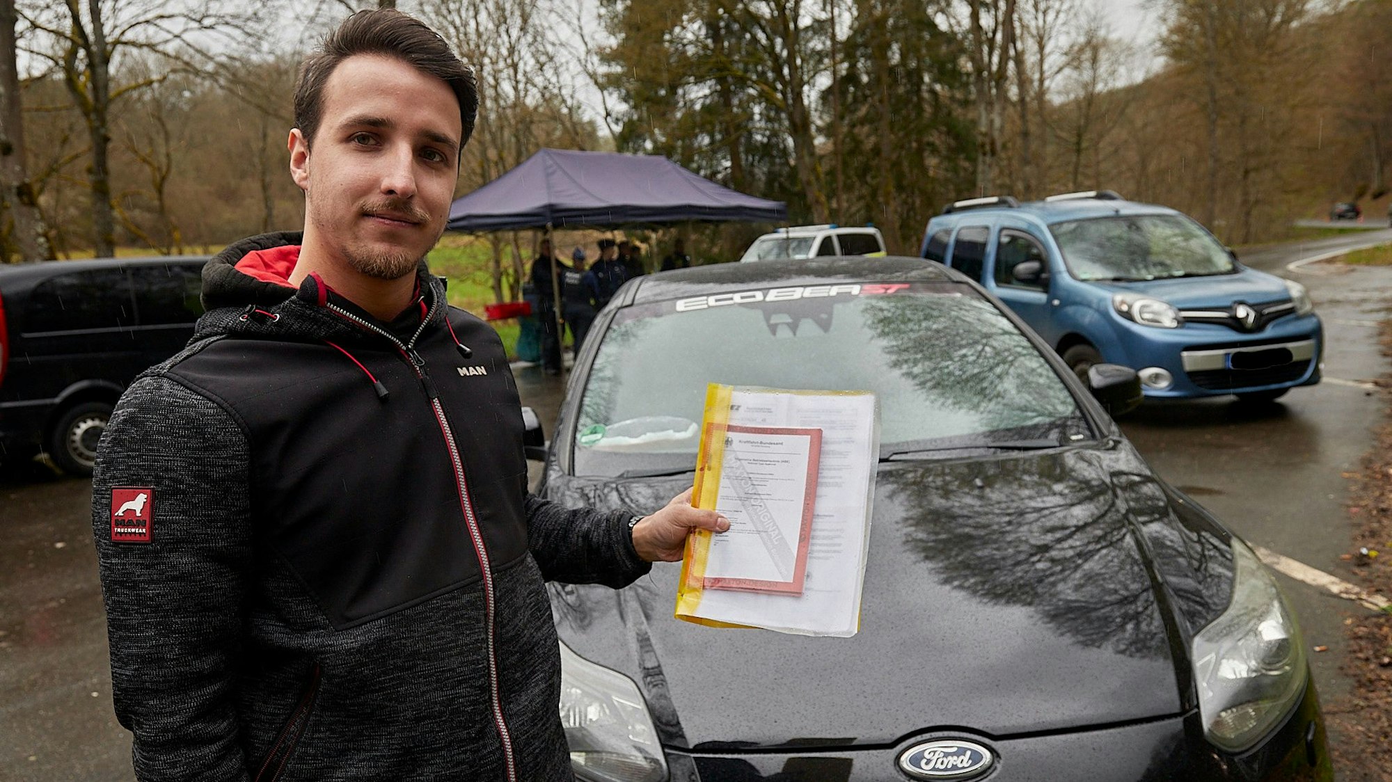 Ein junger Mann steht an seinem getunten Auto. Er hat eine Mappe mit Unterlagen in der Hand, mit denen er alle technischen Veränderungen belegen kann.