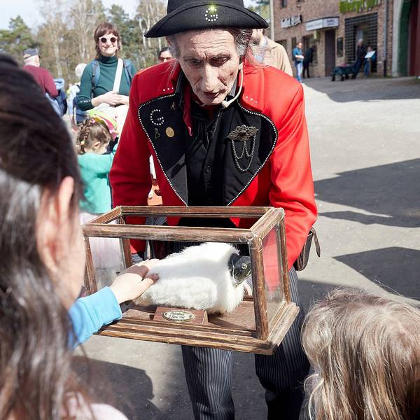 Ein in französischer Uniform gekleideter Mann präsentiert Kindern ein Stofftier in einem Glaskasten.