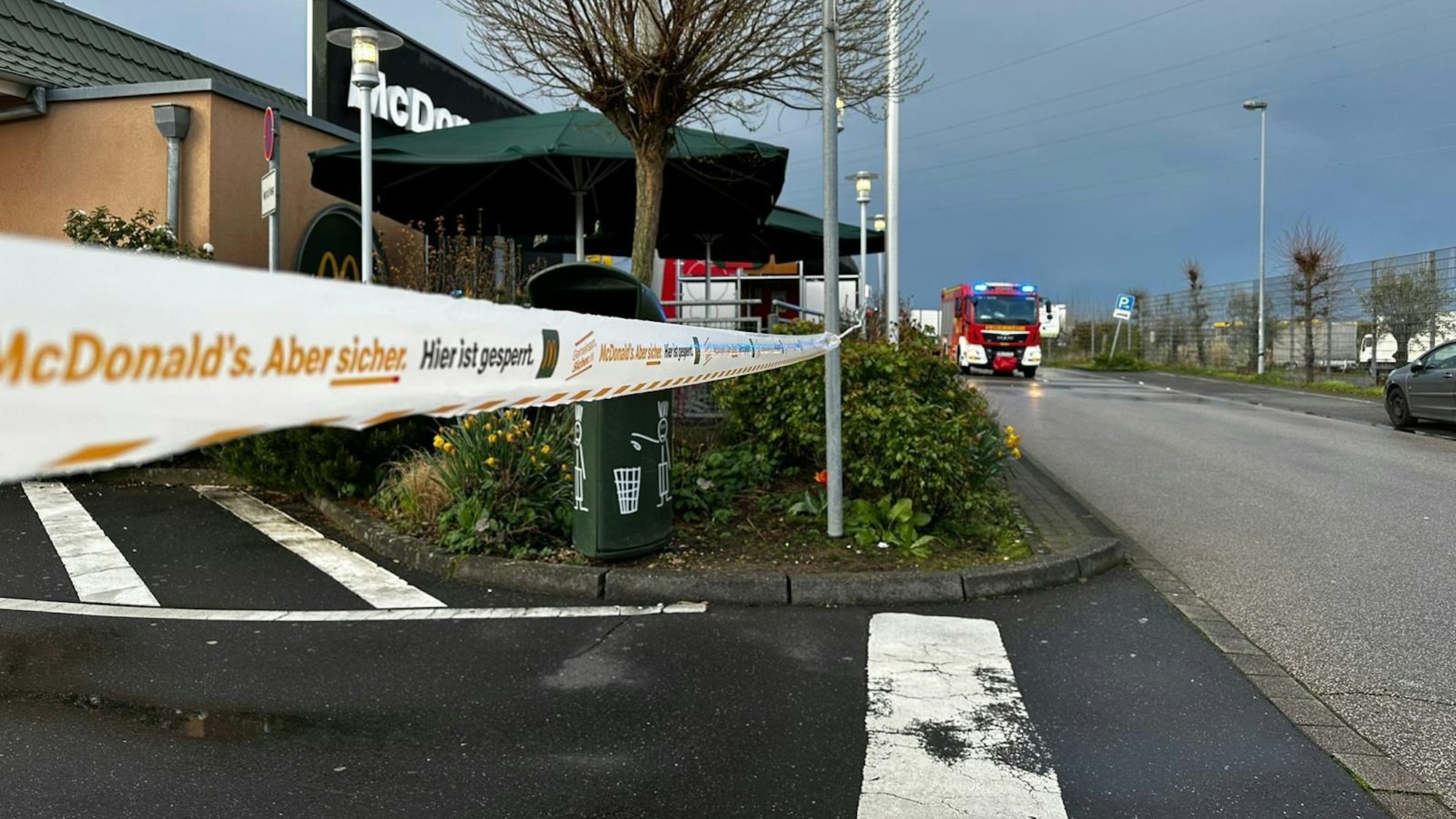Zu sehen ist die abgesperrte Filiale eines Schnellrestaurants, im Hintergrund fährt die Feuerwehr.
